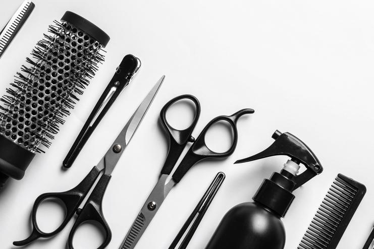 Verschiedene Friseurwerkzeuge, darunter Scheren, Kämme, Bürsten und eine Sprühflasche, ordentlich auf einem weißen Hintergrund angeordnet.