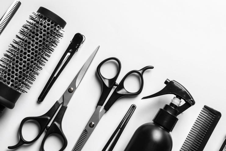 Verschiedene Friseurwerkzeuge, darunter Scheren, Kämme, Bürsten und eine Sprühflasche, ordentlich auf einem weißen Hintergrund angeordnet.