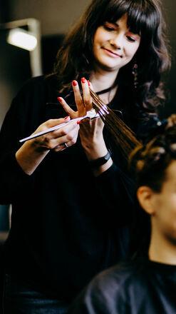 Eine lächelnde Friseurin mit roten Fingernägeln schneidet sorgfältig das Haar einer jungen Kundin in einem modernen Salon.