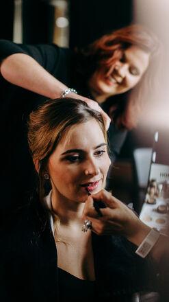 Eine Friseurin arbeitet an der Frisur einer lächelnden Kundin, die im Spiegel betrachtet wird, in einem modernen Friseursalonin Münster..