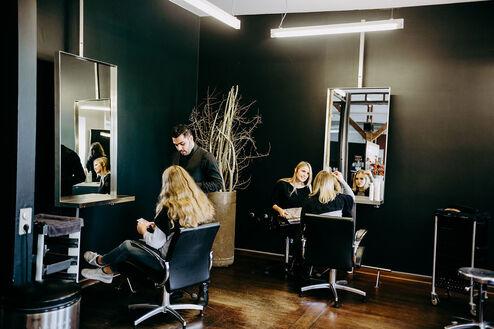 Ein moderner Friseursalon mit Mitarbeitern, die Kunden bedienen. Spiegel reflektieren das geschäftige Treiben im Raum.