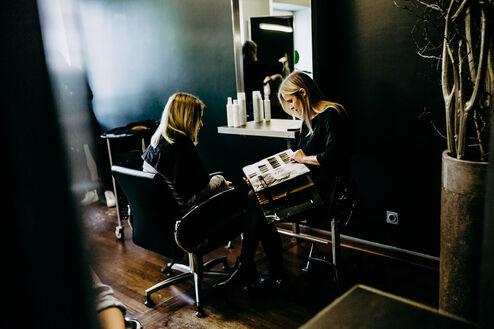 Zwei Frauen auf St&uuml;hlen im Friseursalon bei Beratung