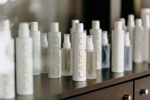 Eine Reihe von weißen Haarpflegeprodukten der Marke CABELO auf einem dunklen Regal, verschwommen im Hintergrund reflektierend.