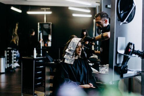Ein Friseur konzentriert sich darauf, Farbe auf die folienbedeckten Haare einer entspannten Kundin in einem modernen Salon aufzutragen.