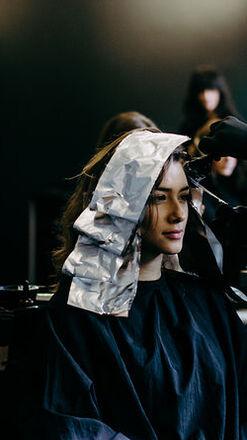 Ein Friseur konzentriert sich darauf, Farbe auf die folienbedeckten Haare einer entspannten Kundin in einem modernen Salon aufzutragen.