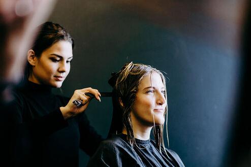 Eine konzentrierte Friseurin trägt Farbe auf das Haar einer jungen Kundin auf, die im Salon entspannt sitzt.