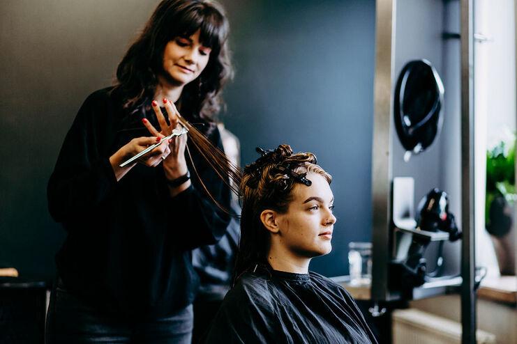 Friseurin stylt Kundin im Salon Eine lächelnde Friseurin arbeitet sorgfältig an der Frisur einer entspannten jungen Kundin in einem modernen Friseursalon.