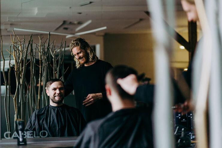 Ein lächelnder Friseur bedient einen zufriedenen Kunden mit einem frischen Herrenhaarschnitt im Friseursalon.