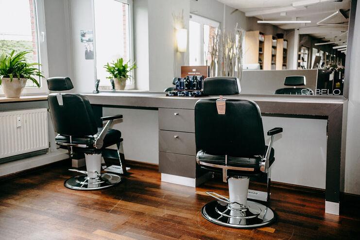 Zwei professionelle Friseurstühle vor großen Spiegeln in einem stilvollen Salon mit Holzboden und Pflanzendekor.