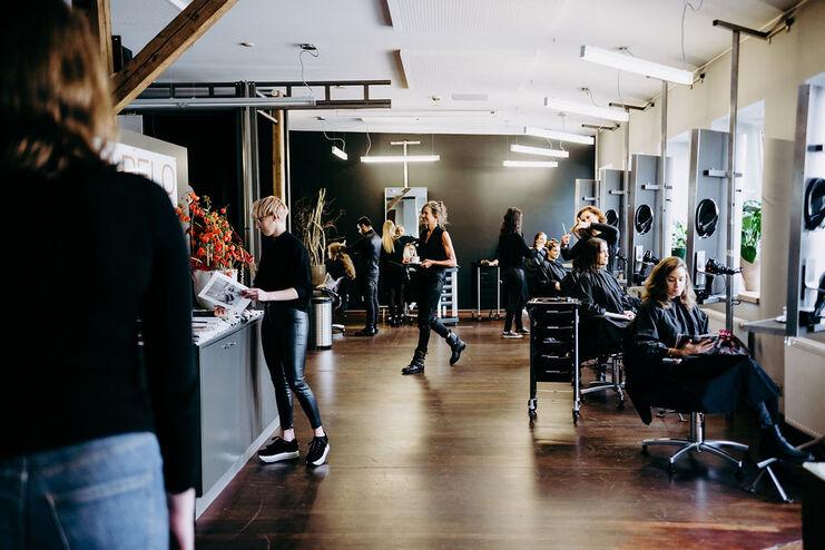 Blick in einen belebten Friseursalon in Münster mit mehreren Kunden und Friseuren, die sich um die Haarpflege kümmern, in einem modern gestalteten Raum.