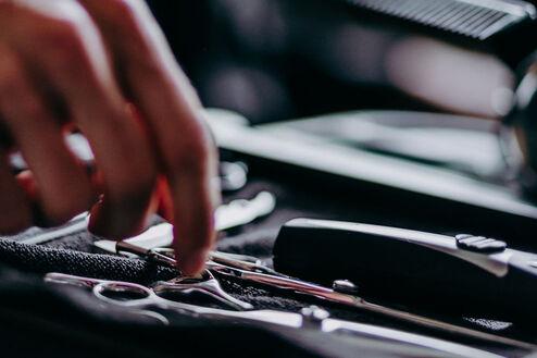 Nahaufnahme von Händen, die Friseurwerkzeuge aus einem offenen, professionellen Werkzeugkoffer in einem Salon auswählen.