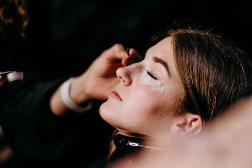 Eine Kosmetikerin trägt sorgfältig eine glitzernde Gesichtsmaske auf das Gesicht einer entspannten Kundin in einem dunklen Salon auf.