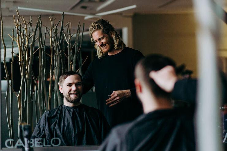 Ein lächelnder Friseur bedient einen zufriedenen Kunden mit einem frischen Herrenhaarschnitt im Friseursalon.
