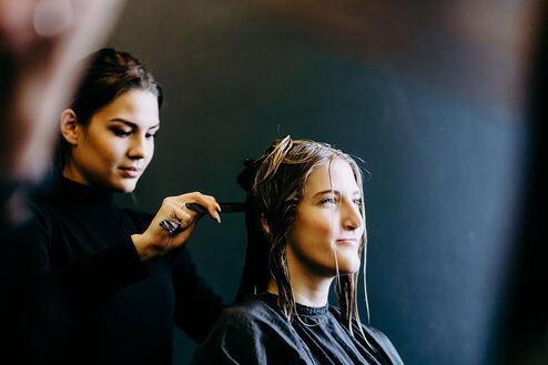 Friseurin färbt Kundin die Haare Eine konzentrierte Friseurin trägt Farbe auf das Haar einer jungen Kundin auf, die im Salon entspannt sitzt.