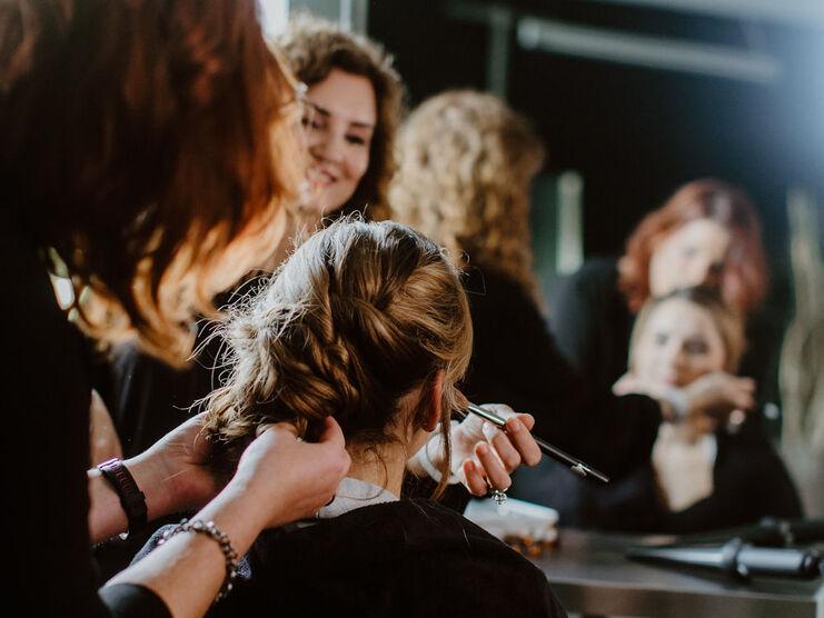 Eine Friseurin gestaltet sorgfältig eine geflochtene Frisur für eine Kundin, die im Spiegel lächelt, in einem Friseursalon in Münster..
