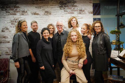 Das Team des Friseurs in Münster und eine Kundin mit lockigem Haar posieren nach einem erfolgreichen Styling-Workshop.