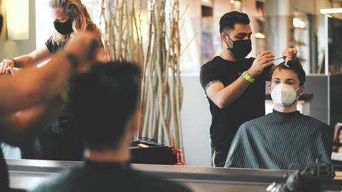 Ein Friseur in Münster schneidet die Haare eines Kunden unter Einhaltung der Hygienemaßnahmen mit Masken.