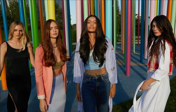 Vier Frauen mit langen Haaren draußen vor bunten Stangen